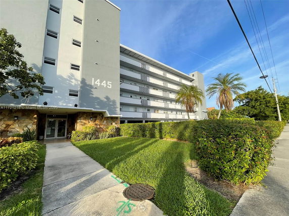 Front view of a multi-story apartment building with a walkway and greenery.