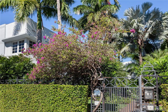 Front view of a house partially obscured by palm trees and a gated fence.
