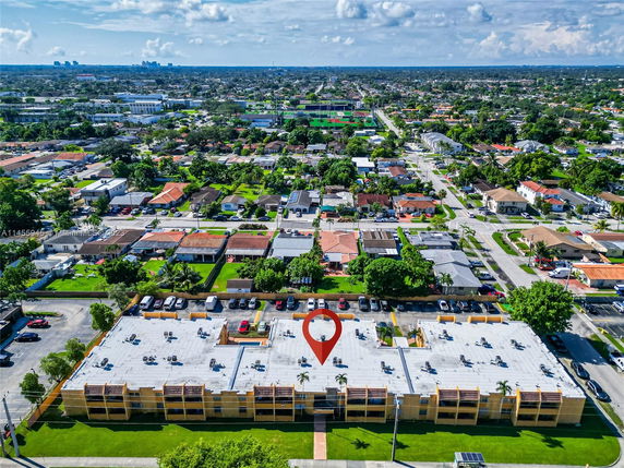 Aerial view of a residential area with multiple houses and a prominent flat-roofed apartment building in the foreground.