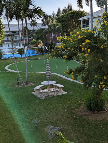 Outdoor view featuring a putting green and surrounding garden area with buildings in the background.