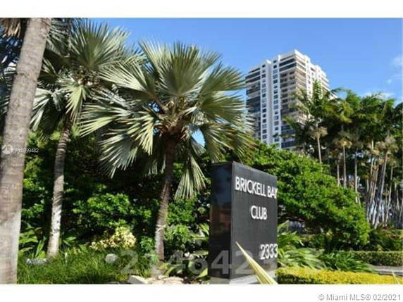 View of a sign for Brickell Bay Club with high-rise buildings and palm trees in the background.