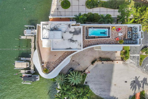 Aerial view of a building with a rooftop featuring a pool, seating area, and air conditioning units next to a waterfront.