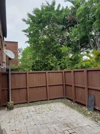 Outdoor view of a fenced patio area with a satellite dish and surrounding trees.