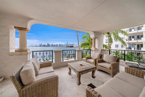 Spacious balcony with wicker furniture and a view of the ocean and city skyline.