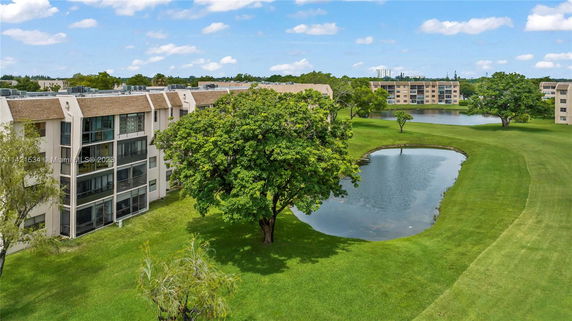 View of apartment buildings with a tree and pond in the foreground.
