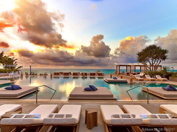 Outdoor swimming pool area with lounge chairs and ocean view at sunset.