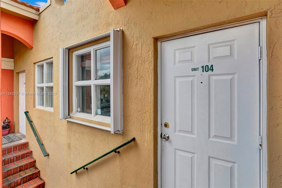 Front view of a building with stairs leading to entrance door marked Unit 104.