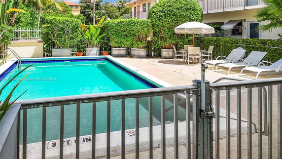 Outdoor swimming pool area with lounge chairs and a table under an umbrella.