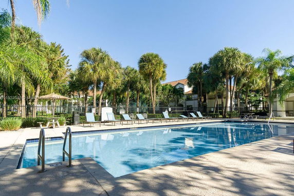 Outdoor swimming pool with surrounding palm trees and lounge chairs.