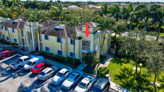 Front view of a yellow multi-story residential building with parking area in front.