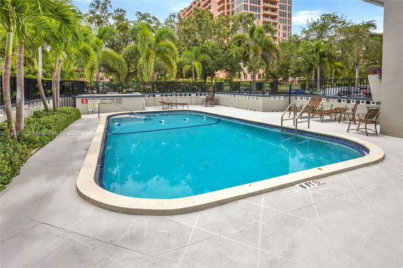 Outdoor swimming pool with surrounding lounge chairs and tropical plants.