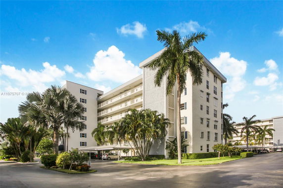 Front view of a multi-story apartment building with balconies and a covered parking area.