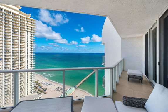 Panoramic view from a balcony overlooking the ocean and beach with a nearby high-rise building.