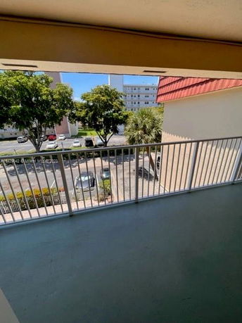 View from a balcony showing a parking area and buildings with trees.