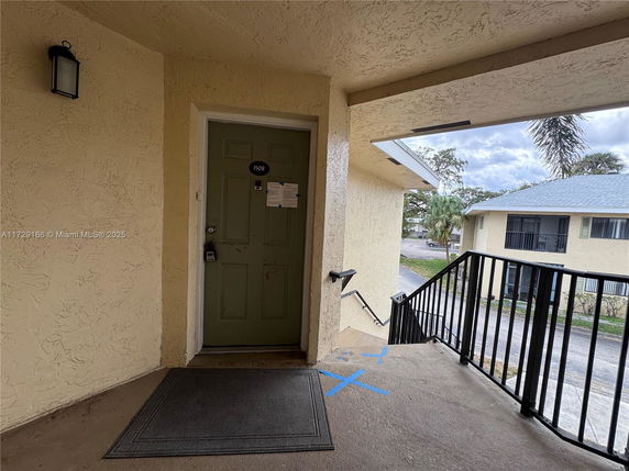Entrance to a residential building with a green door, external staircase and view of neighboring building.