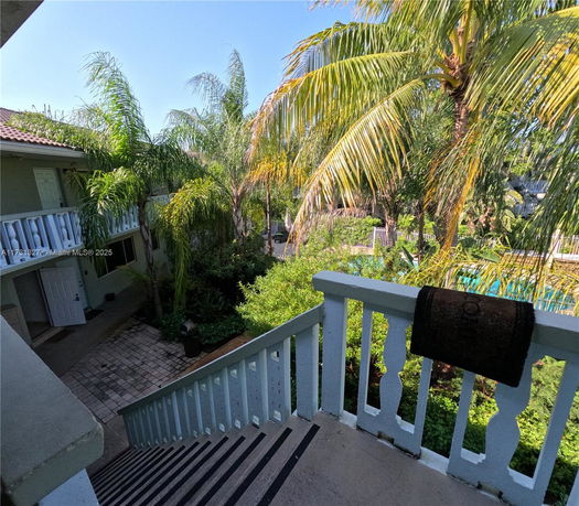 View from a staircase overlooking a lush, tropical courtyard with palm trees and a glimpse of a building entrance.
