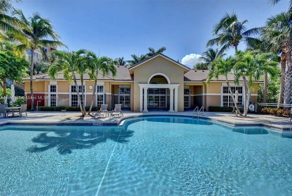 Front view of a one-story building with large windows and a gabled roof, situated by a swimming pool.