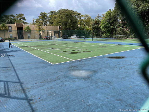 Tennis court with puddles after rain, surrounded by trees and buildings.