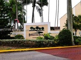 Front view of a building with a sign reading 'Hammocks Trails Condos' surrounded by palm trees.