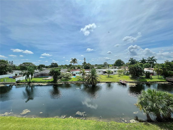 Panoramic view of a residential area with houses, greenery, and a pond under a blue sky.