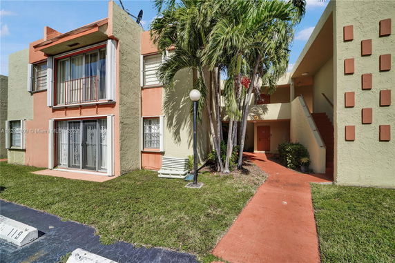 Front view of a multi-story apartment building with balconies and tropical landscaping.