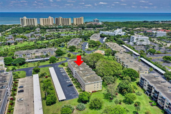 Aerial view of several multi-story buildings near the ocean, surrounded by greenery and parking lots.