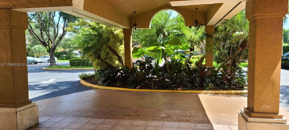 Outdoor approach of a building entrance with columns and greenery.