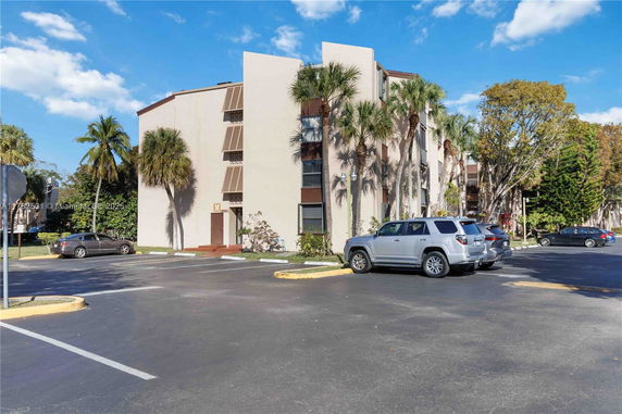 Parking area in front of a multi-story building with palm trees nearby.