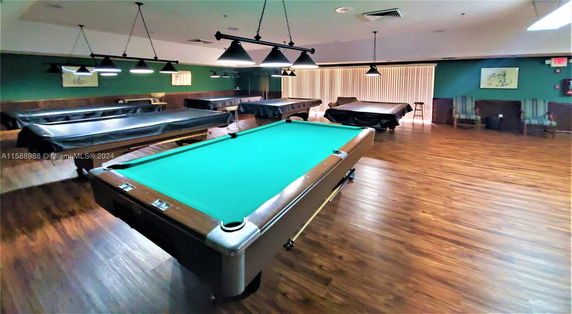 Indoor recreation room with multiple billiard tables and wooden flooring.