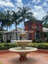 Front view of a two-story brick house with palm trees and a fountain in front.
