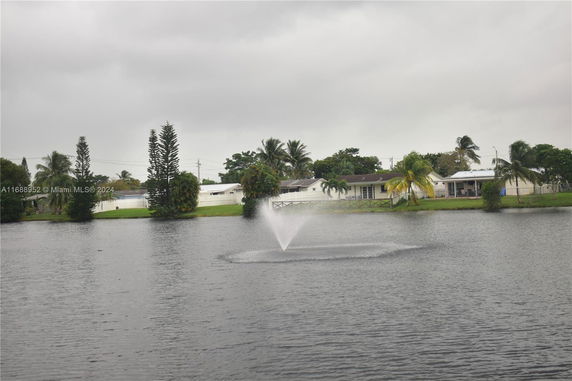 Houses with a white fence and trees near a body of water with a fountain.