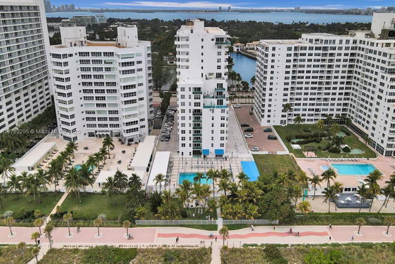 Aerial view of multiple high-rise apartment buildings near a water body with several swimming pools and landscaped areas.