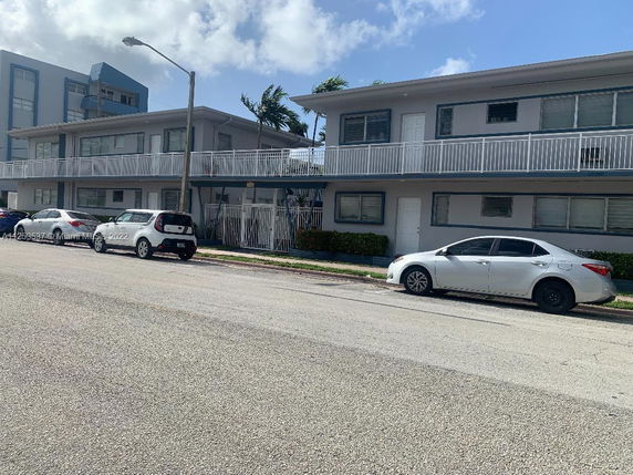 Front view of a two-story apartment building with parked cars along the street.
