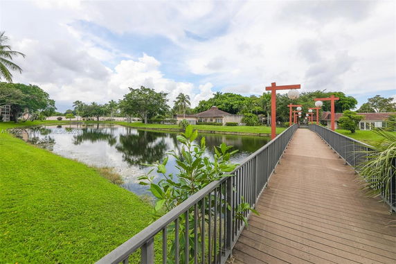 Bridge over a pond with surrounding greenery leading to residential buildings.
