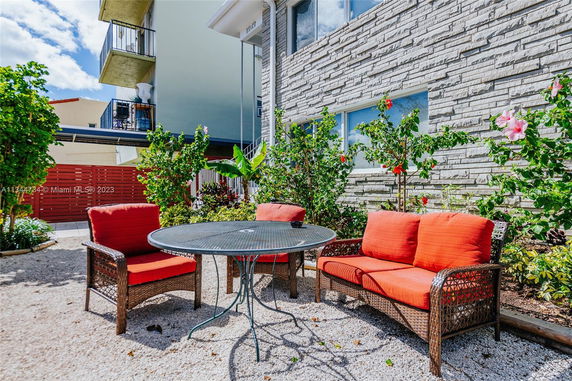 Outdoor seating area with a round table and cushioned chairs, adjacent to a building with a stone facade.