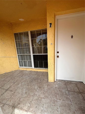 Front view of a building entrance with a tiled porch area and a white door.