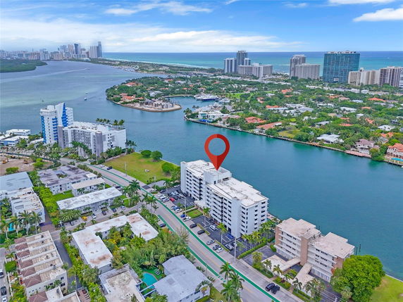 Aerial view of a riverside apartment complex in an urban area, surrounded by water and greenery.