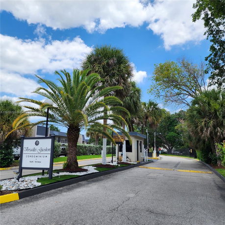 Entrance view of a condominium complex with a driveway and palm trees.