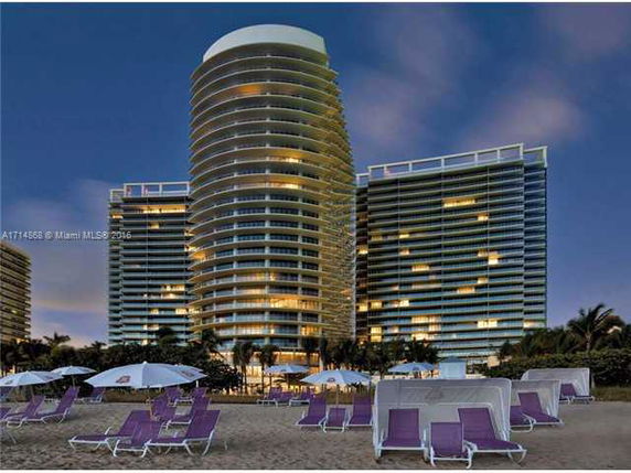 Cluster of illuminated high-rise buildings viewed from the beach at dusk.