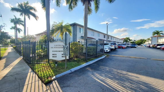 Front view of a two-story apartment building with a parking area and surrounding palm trees.