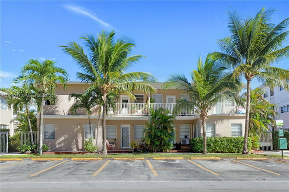 Front view of a two-story building with balconies and palm trees.