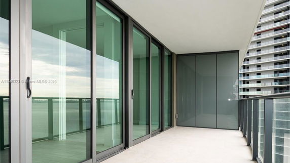 Balcony view with glass sliding doors and railing, overlooking water and adjacent buildings.