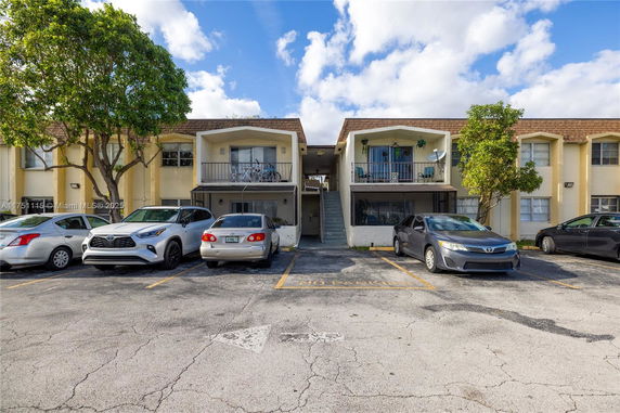 Front view of an apartment building with balconies and parked cars.