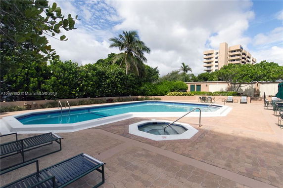 View of a swimming pool area with lounge chairs and a building in the background.
