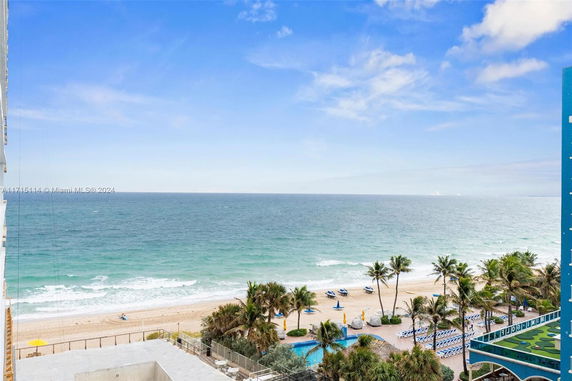 Wide-angle view of the ocean and beachfront with palm trees and sun loungers.
