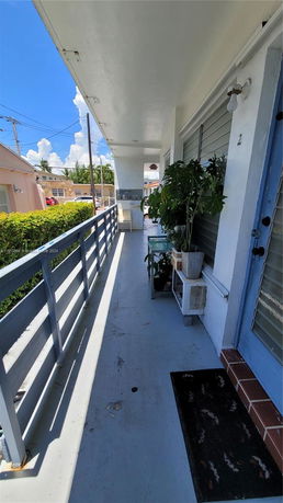 Outdoor corridor of a building with plants and railings, adjacent to residential structures.