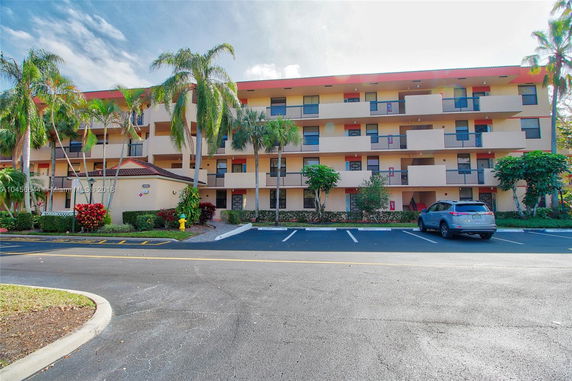 Front view of a multi-story building with balconies and a parking area.
