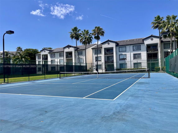 View of a tennis court in front of a multi-story residential building.