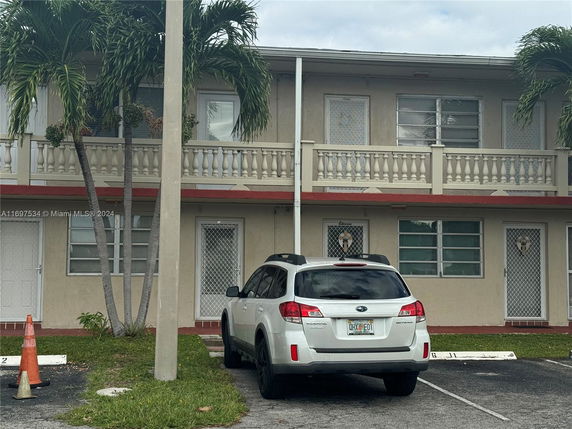 Two-story building with parking space in front, featuring a parked vehicle and palm trees.