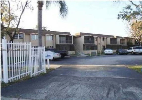 Front view of a multi-unit building with parking area and gated entrance.